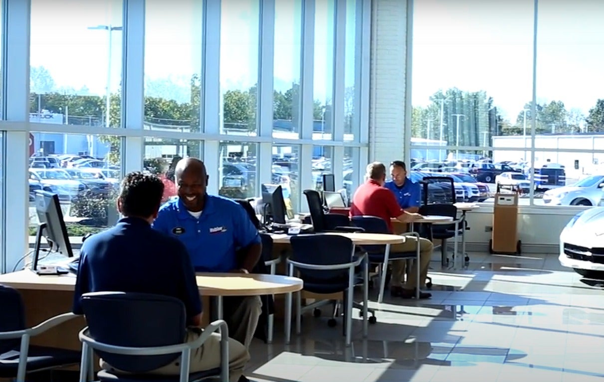 image of a salesmen and custonmers at desks inside of a dealership